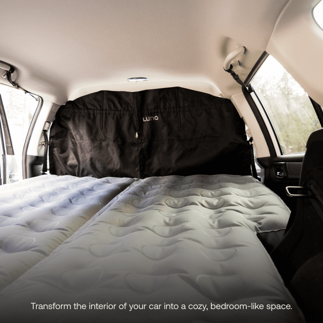 Transform your car's interior into a cozy, bedroom-like space with a fitted air mattress covering the back section. A stylish Car Privacy Curtain from Luno HQ in sleek black hangs behind the front seats.