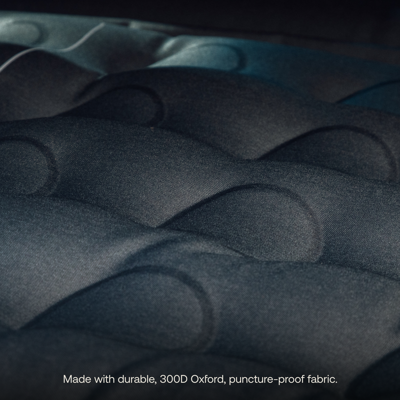 Close-up image of the black, cushioned surface of the Luno® AIR Van Front Cab Mattress, crafted from durable 300D Oxford, puncture-proof fabric. The text at the bottom reads, "Made with durable 300D Oxford, puncture-proof fabric for extra sleeping space.