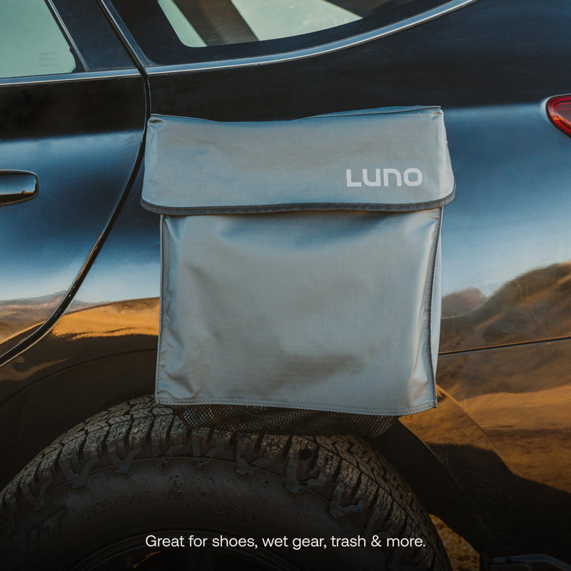 A blue "Luno HQ" Gear & Shoe Storage Bag (Pre-Owned) is attached to the side of a glossy black car over the rear wheel. Ideal for shoes, pre-owned gear, trash & more. The blurred background highlights this practical accessory. Benefit from convenient USA shipping on every order.