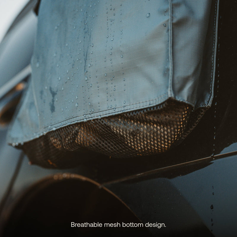 Image of a car window with a waterproof cover partially wet with raindrops. The cover features a breathable mesh bottom, similar to Luno HQ's Gear & Shoe Storage Bag (Pre-Owned). The black car is the focal point against the soft background. Text reads: "Breathable mesh bottom design.